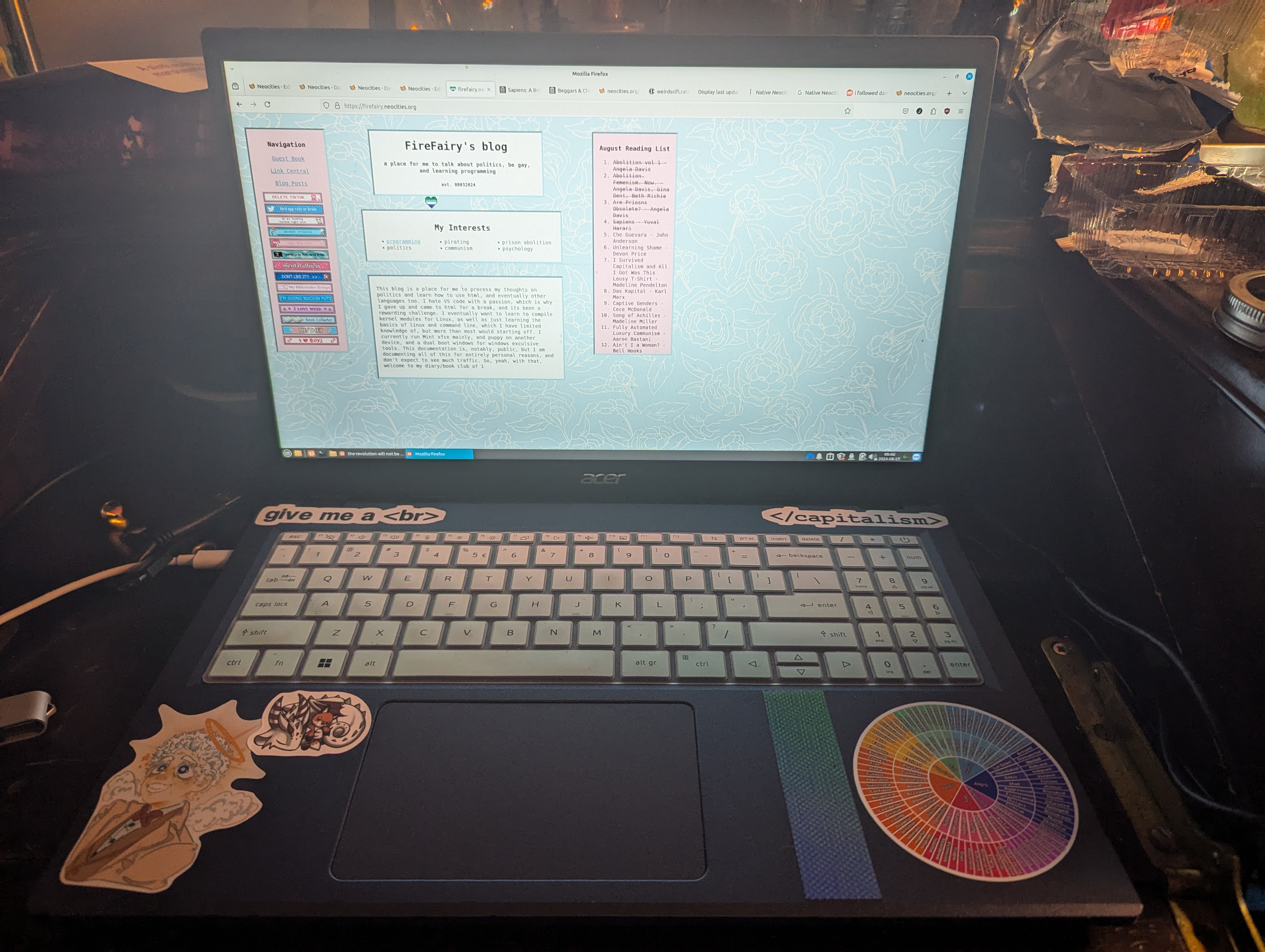 The inside of a blue Acer Aspire 3 15 with a pale blue silicone keyboard cover, above the keyboard is 2 html stickers, below the keyboard, on the left of the trackpad, is a sticker of Aziraphael from Good Omens, and a sticke rof a dragon curled up alseep with a fox plush, on the right of the track pad is a textured stim sticker and a emotion wheel sticker